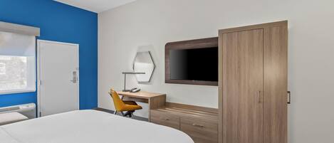 Une chambre d’hôtel équipée d’un lit, d’un bureau, d’une chaise, d’une armoire et d’un téléviseur fixé au mur.