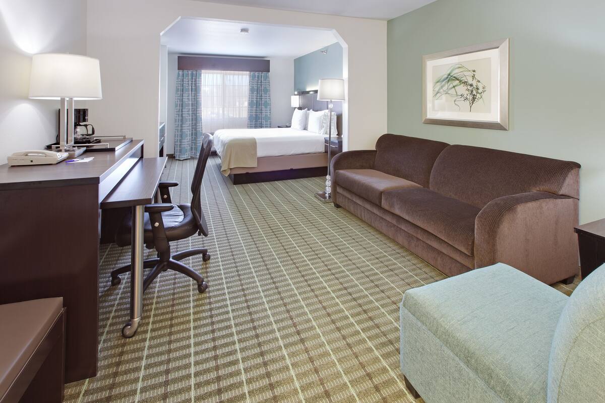 A hotel room with a bed, a desk, a chair, a sofa, and a framed picture on the wall.