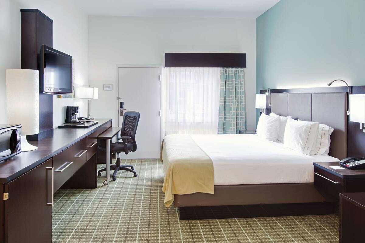 A hotel room with a bed, desk, chair, and a television.