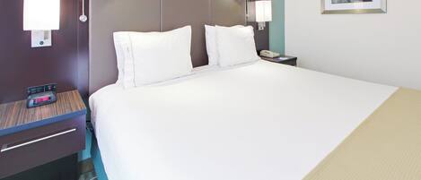 A hotel room with a large bed, two bedside tables, a nightstand, a lamp, a clock, and a painting on the wall.