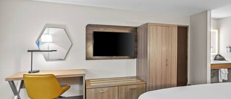 A hotel room with a bed, a desk with a chair, a TV mounted on the wall, and a wardrobe.