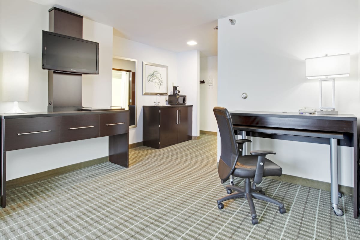 A hotel room with a desk, chair, flat-screen TV, cabinet, and a framed picture on the wall.