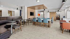 A modern dining area with a mix of seating options including a long communal table and individual chairs, a sofa, and small round tables. - Holiday Inn Express Monticello by IHG (Monticello)