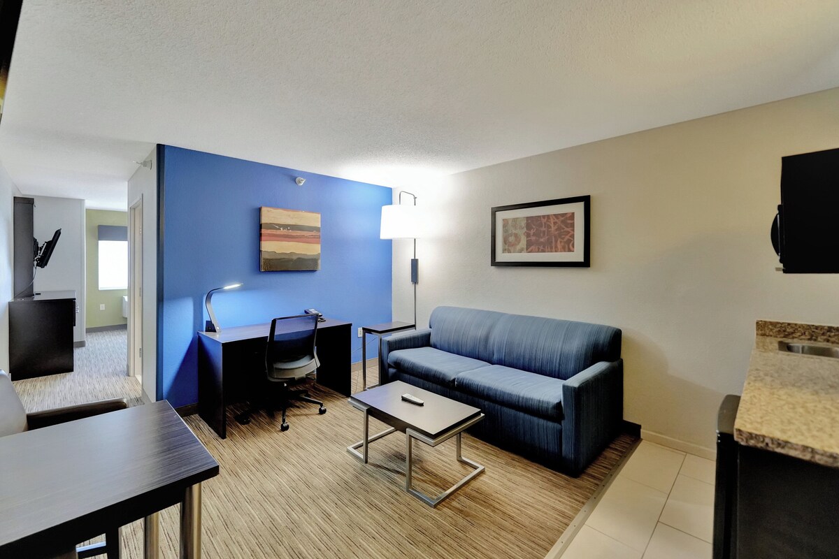 A modern living room with a blue accent wall, a sofa, a desk with a chair, a coffee table, and a lamp.