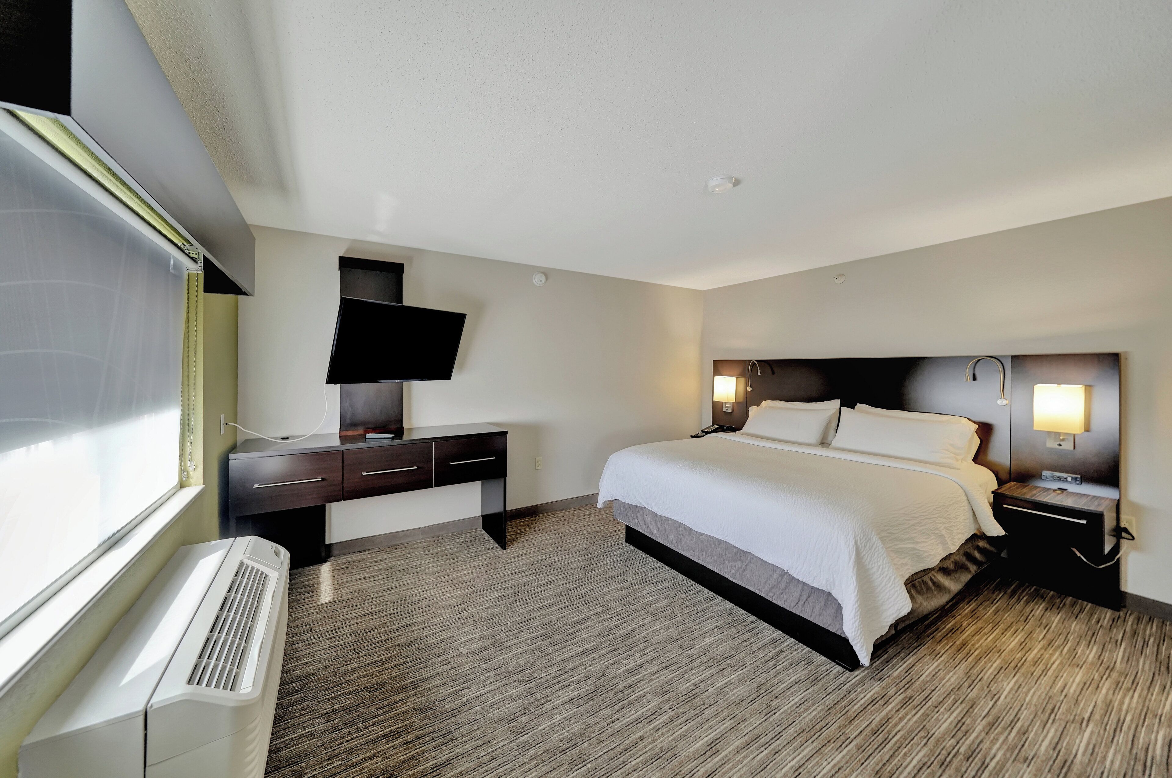 Habitación de hotel con cama, mesitas de noche, televisión de pantalla plana, escritorio y ventana.