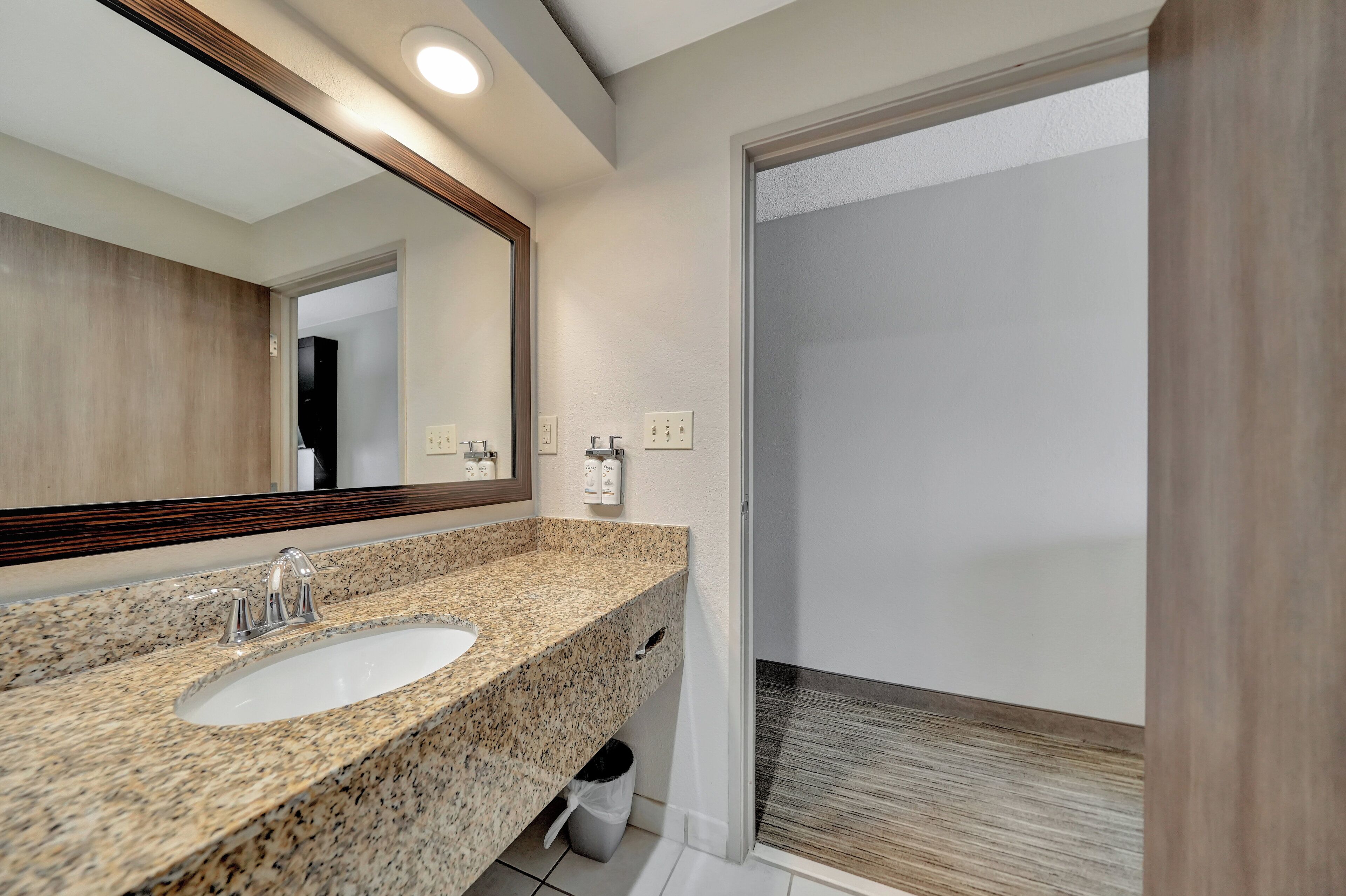 Baño con lavamanos de encimera de granito, espejo y zona de ducha.