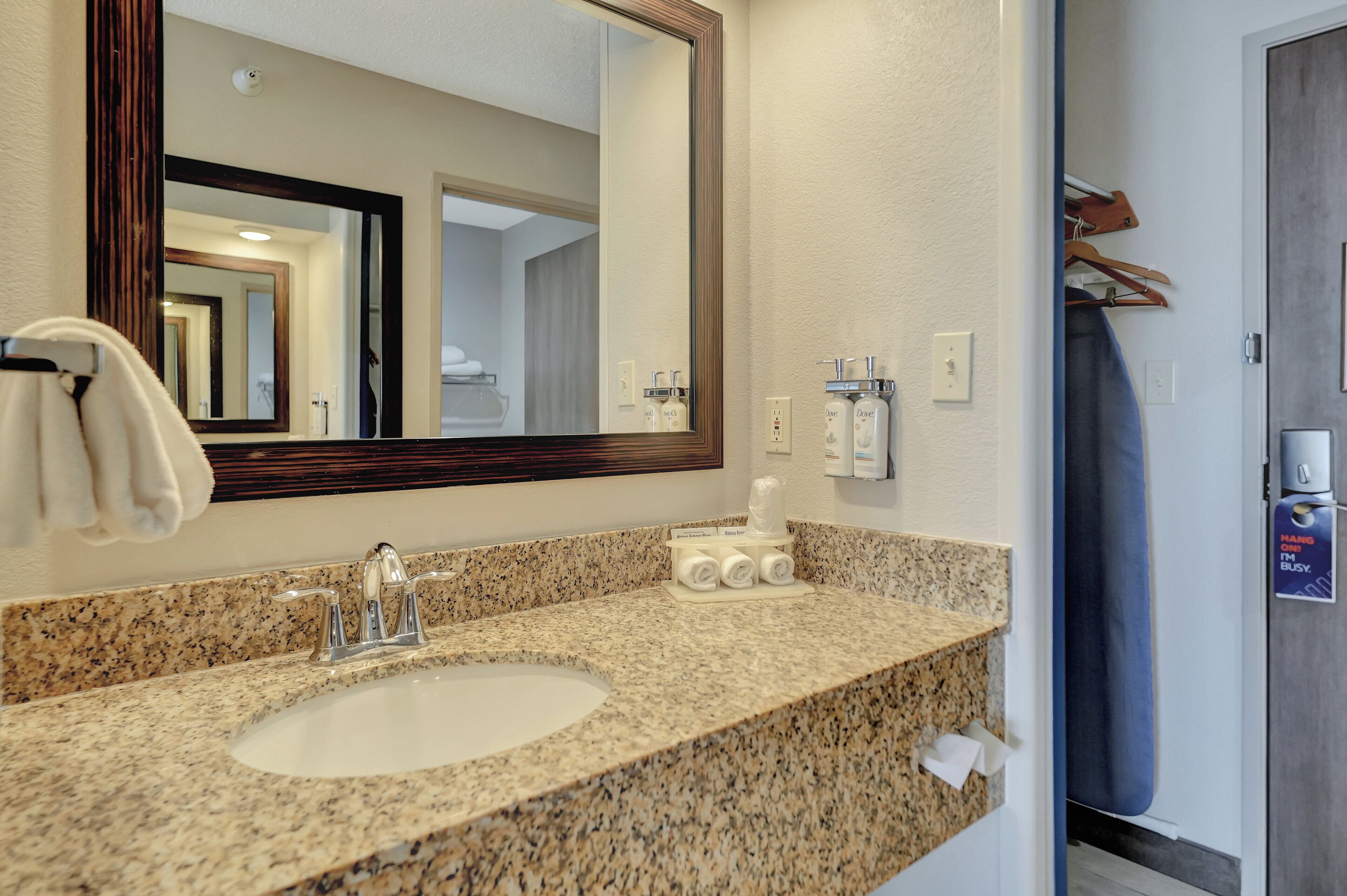A bathroom with a granite countertop sink, a large mirror, and a towel rack.