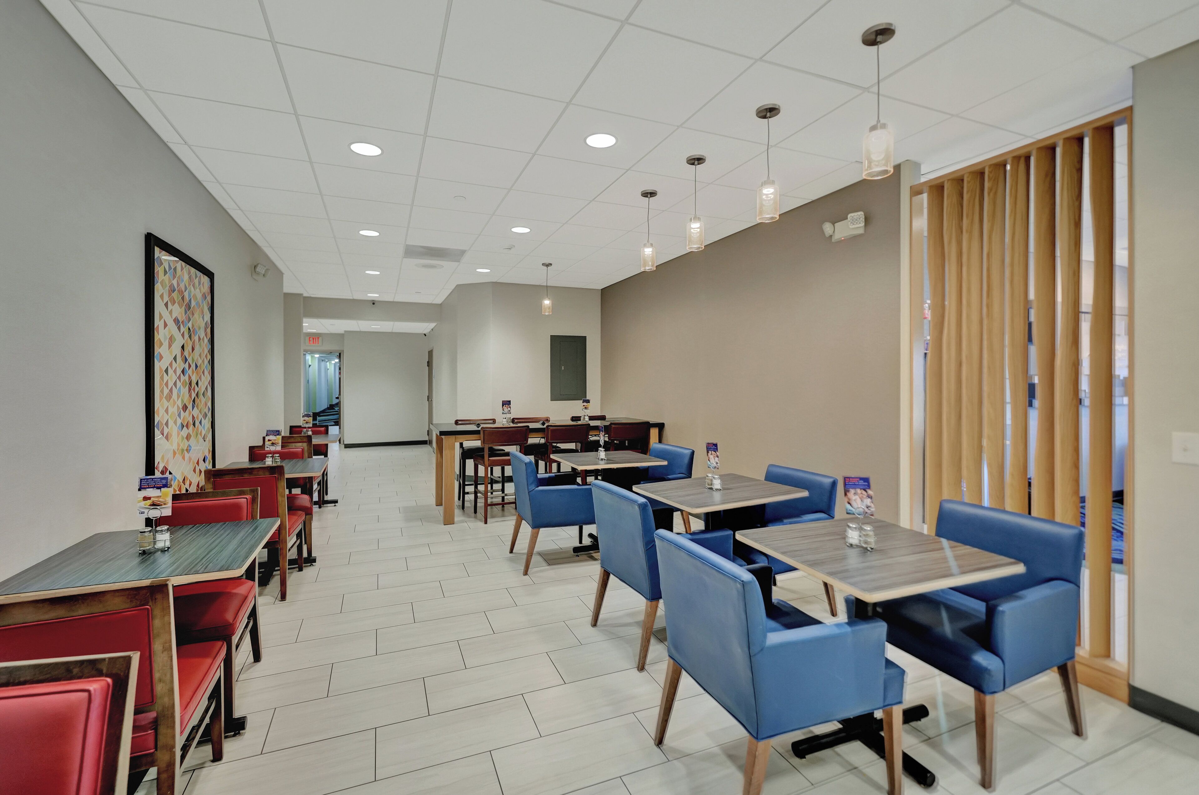 A modern dining area with red and blue booths and tables, wooden partitions, and a tiled floor.