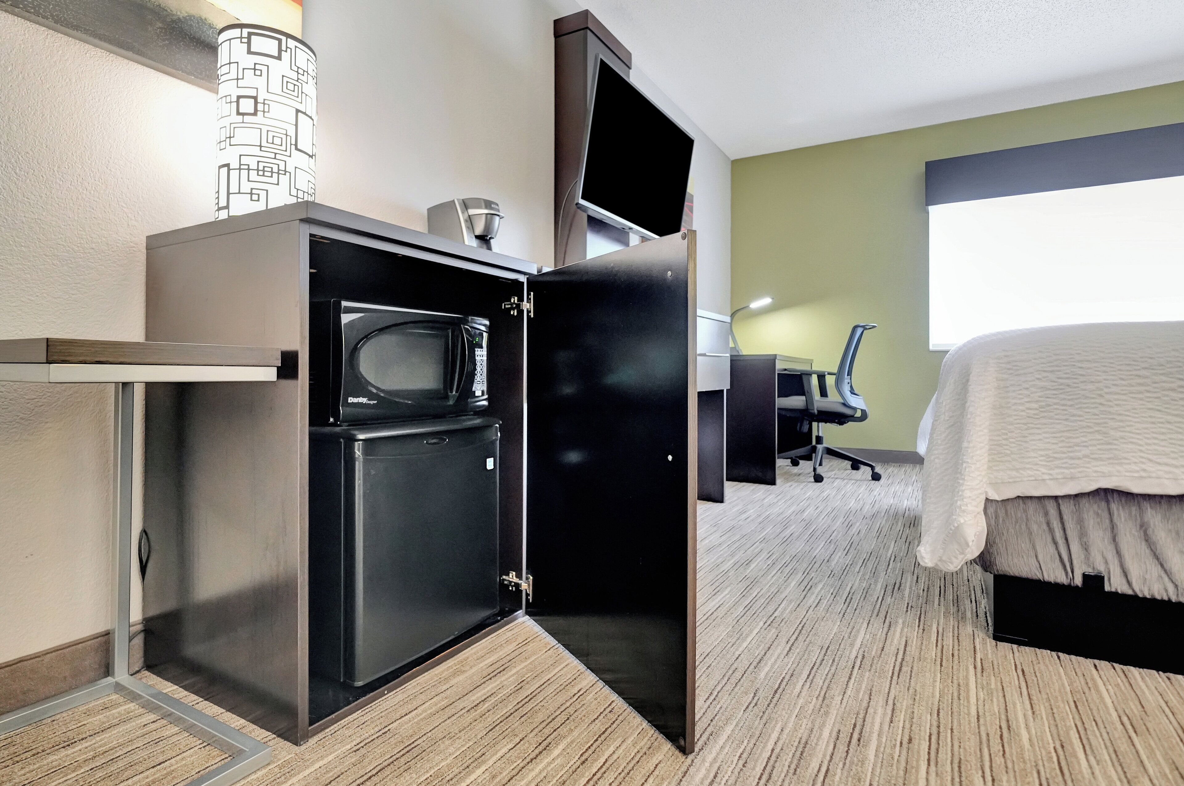 Habitación de hotel pequeña con kitchenette, una cama, un escritorio y un ventanal grande.