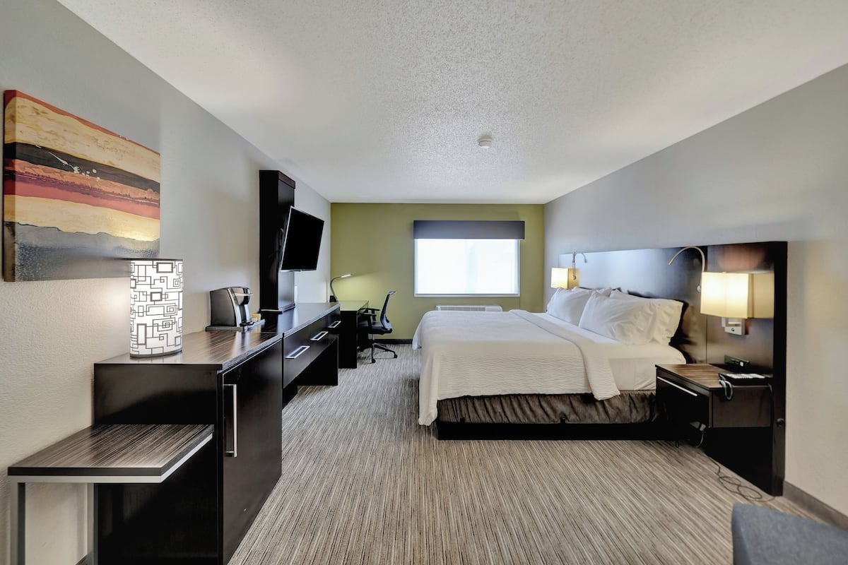 A hotel room with a bed, desk, chair, TV, lamp, and artwork on the wall.