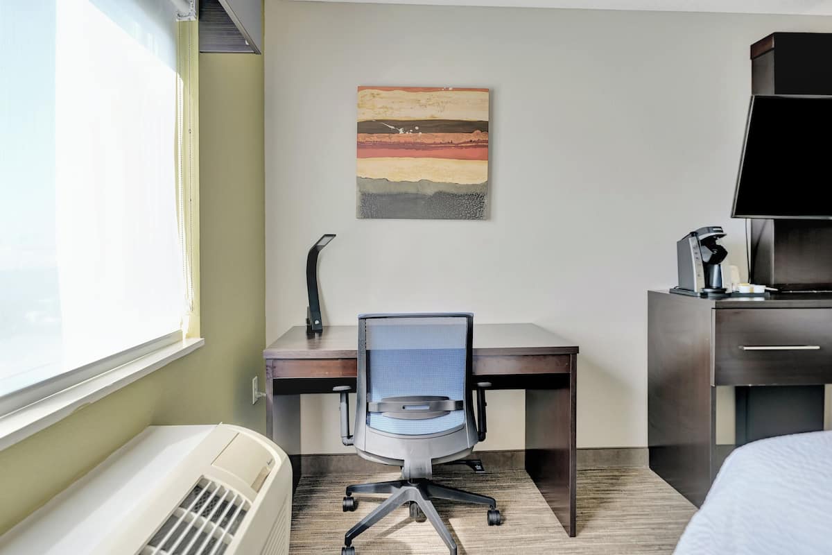 A hotel room with a desk, chair, and a large window.