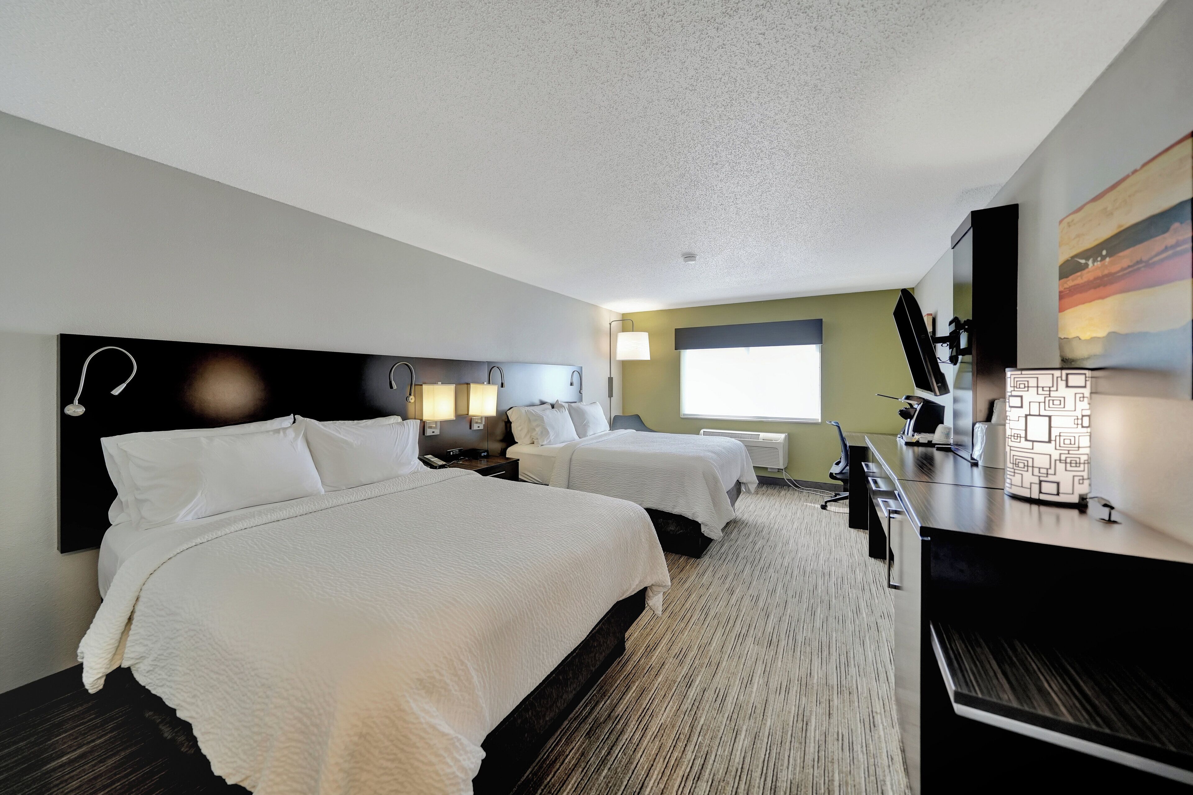A hotel room with two beds, a desk, a TV, and a window.
