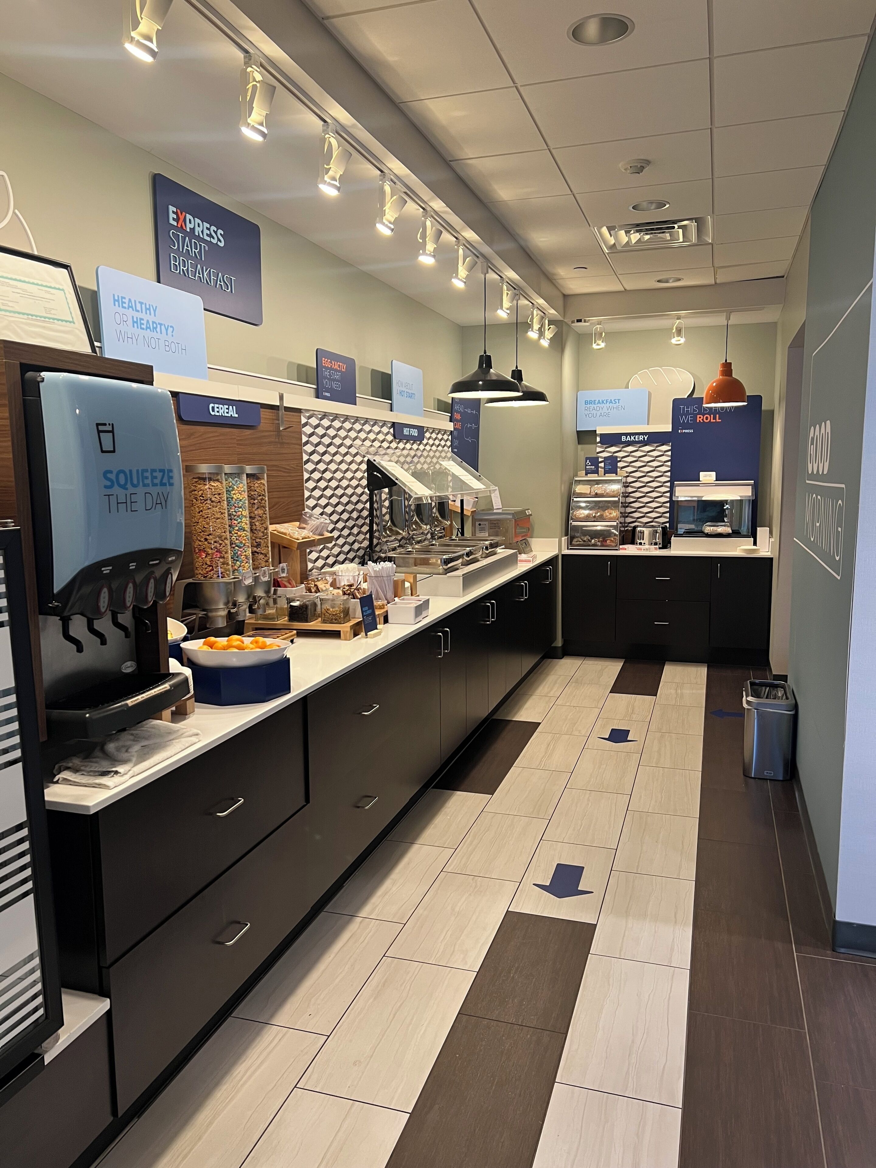 A breakfast area with a self-serve station, cereal and fruit options, and a bakery section.