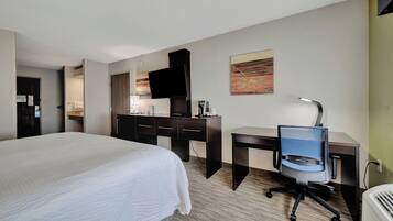 A hotel room with a large bed, a desk with a chair, a flat-screen TV, and a coffee machine.