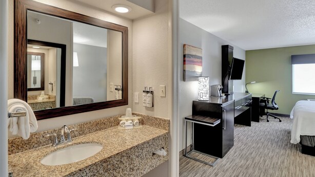 A hotel bathroom with a granite countertop sink, a large mirror, and a towel rack.