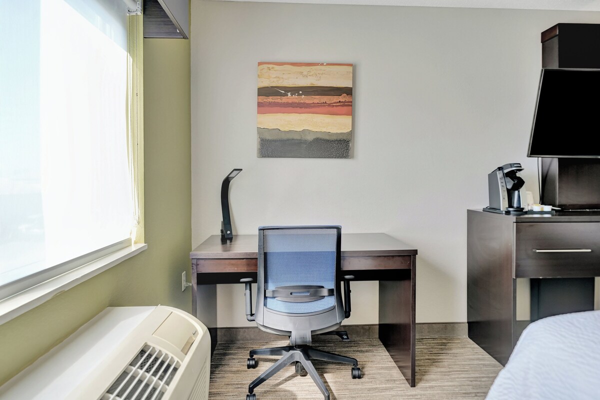 A hotel room with a desk, chair, and a large window.