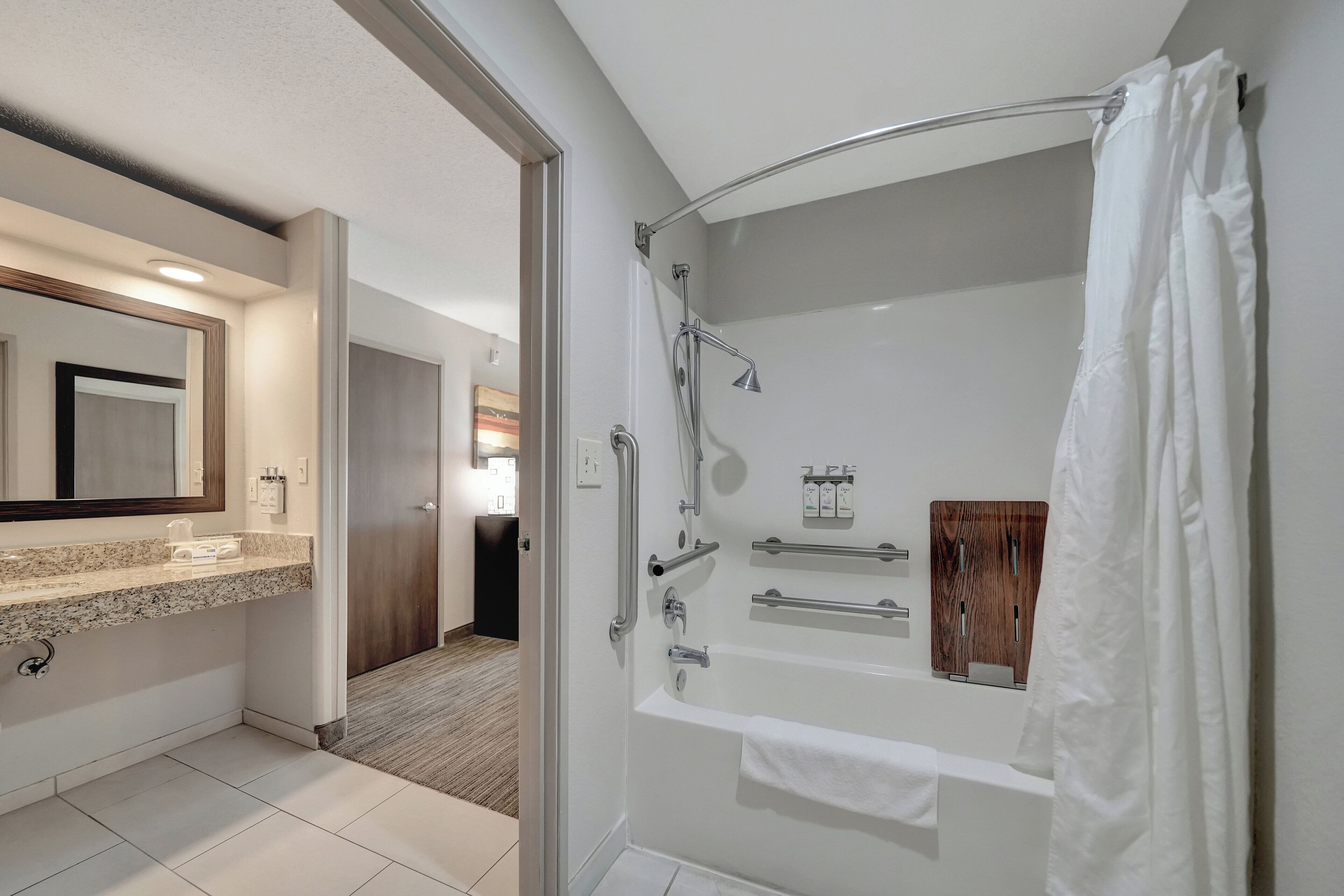 Une salle de bain moderne dotée d’une douche à l’italienne, d’un meuble-lavabo avec un plan de travail en granit et d’un grand miroir.