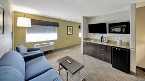 A modern living room with a sofa, a small table, and a kitchen area with a microwave and refrigerator.