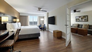 A hotel room with a large bed, a desk with a chair, a TV, a ceiling fan, and a view of the city through the window. - Courtyard Charleston Historic District (Charleston)