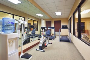 Un gimnasio con equipo de ejercicio, dispensador de agua y espejo.