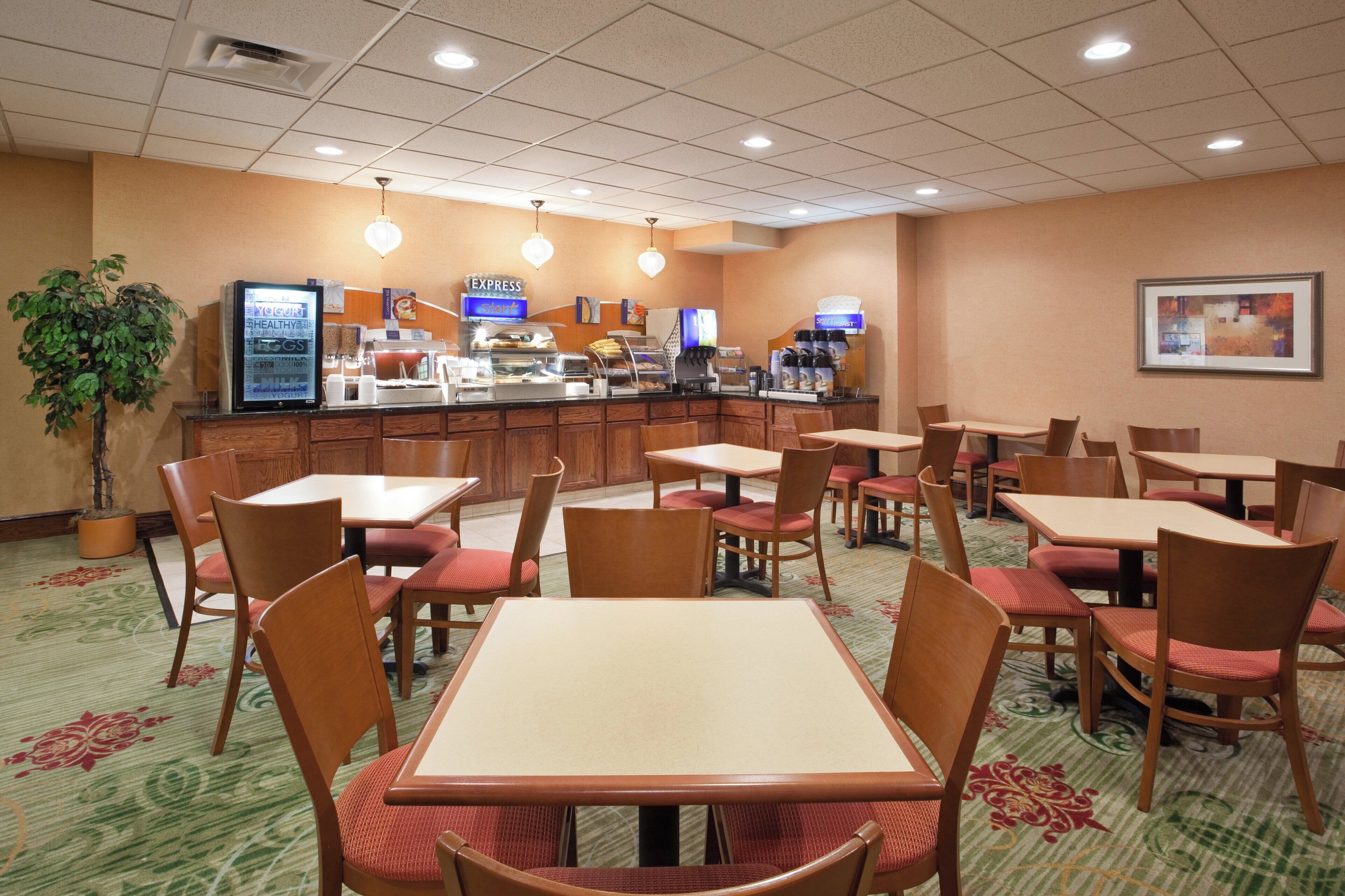 Un comedor de hotel con varias mesas y sillas, un mostrador de buffet y una estación de café.