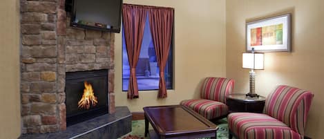 A living room with a fireplace, a television mounted above it, striped armchairs, a small table, and a framed picture on the wall.