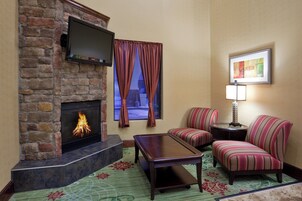 Una sala de estar con chimenea, un televisor montado sobre ella, sillones a rayas, una mesita y un cuadro en la pared.