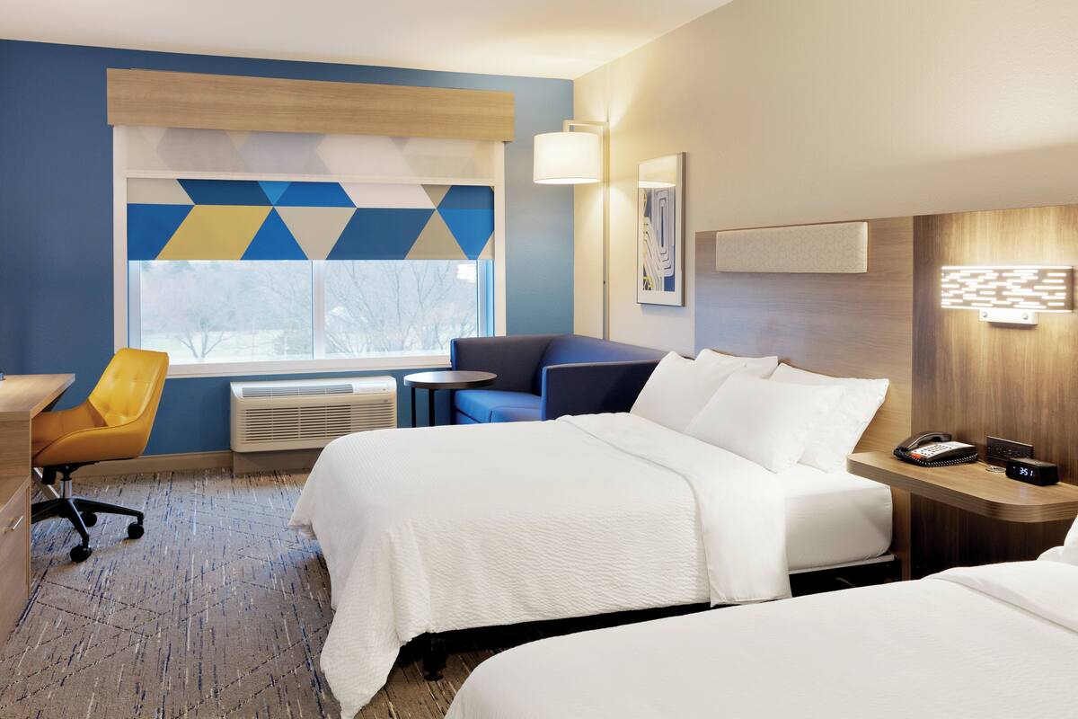 A hotel room with two beds, a desk, a chair, a small table, and a window with a view.