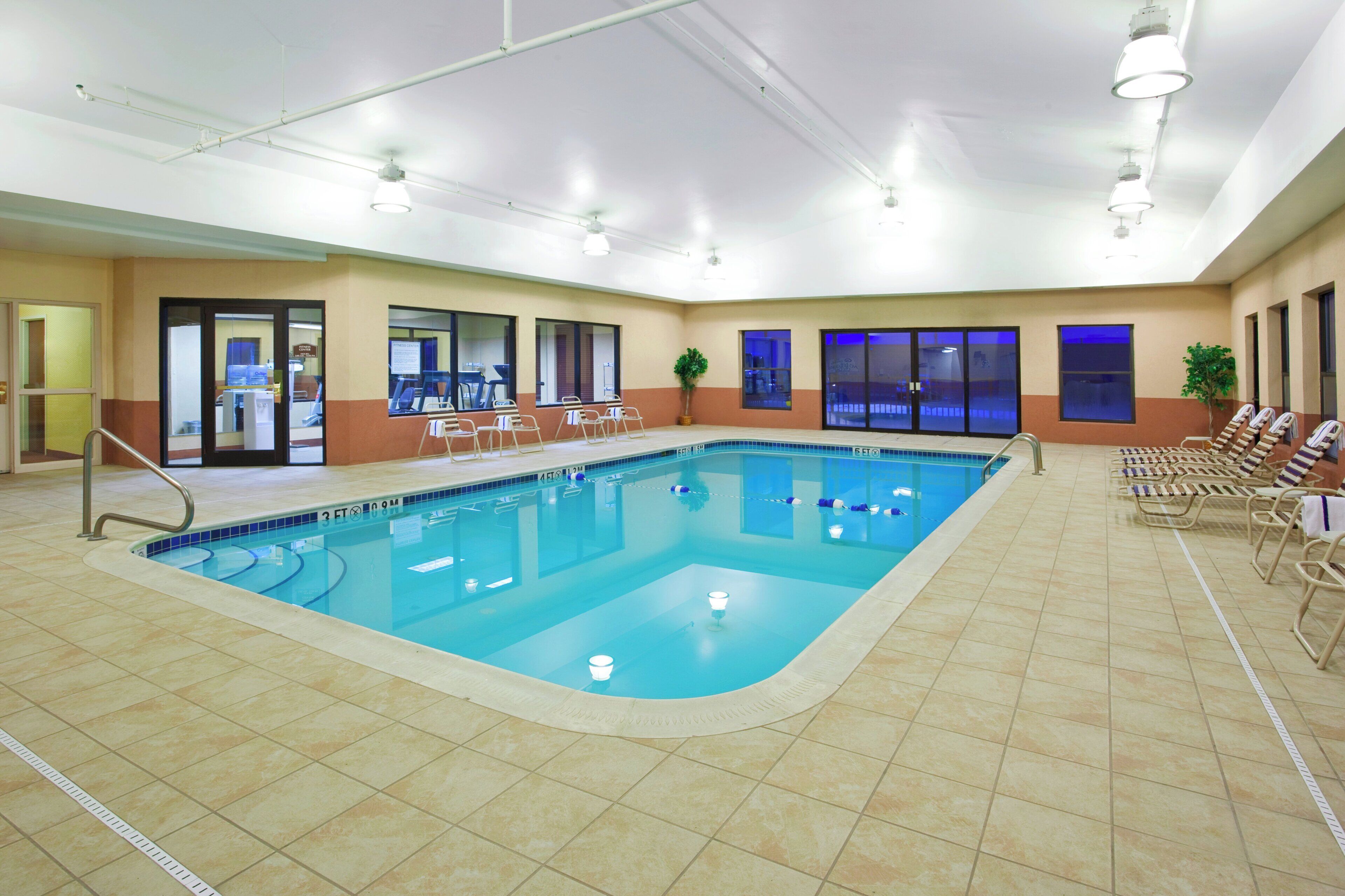 An indoor swimming pool with clear lane markings, a lifeguard chair, and a seating area with chairs.