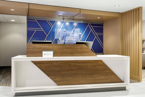 A reception desk with a modern design, featuring a wooden accent and a blue geometric wall behind it. - Holiday Inn Express Hotel & Suites Cleveland-Streetsboro by IHG (Streetsboro)