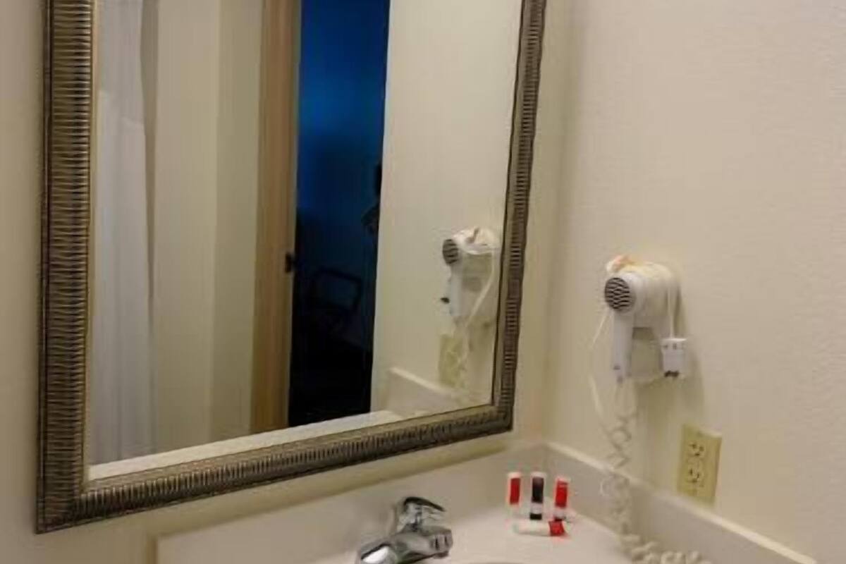 Un baño con un espejo grande, un lavabo, un secador de pelo y un perchero para toallas.