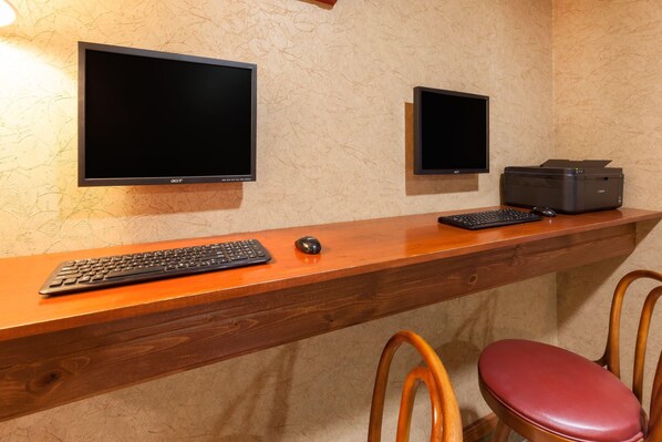 A wooden desk with a keyboard, mouse, and printer, two monitors, and two chairs.