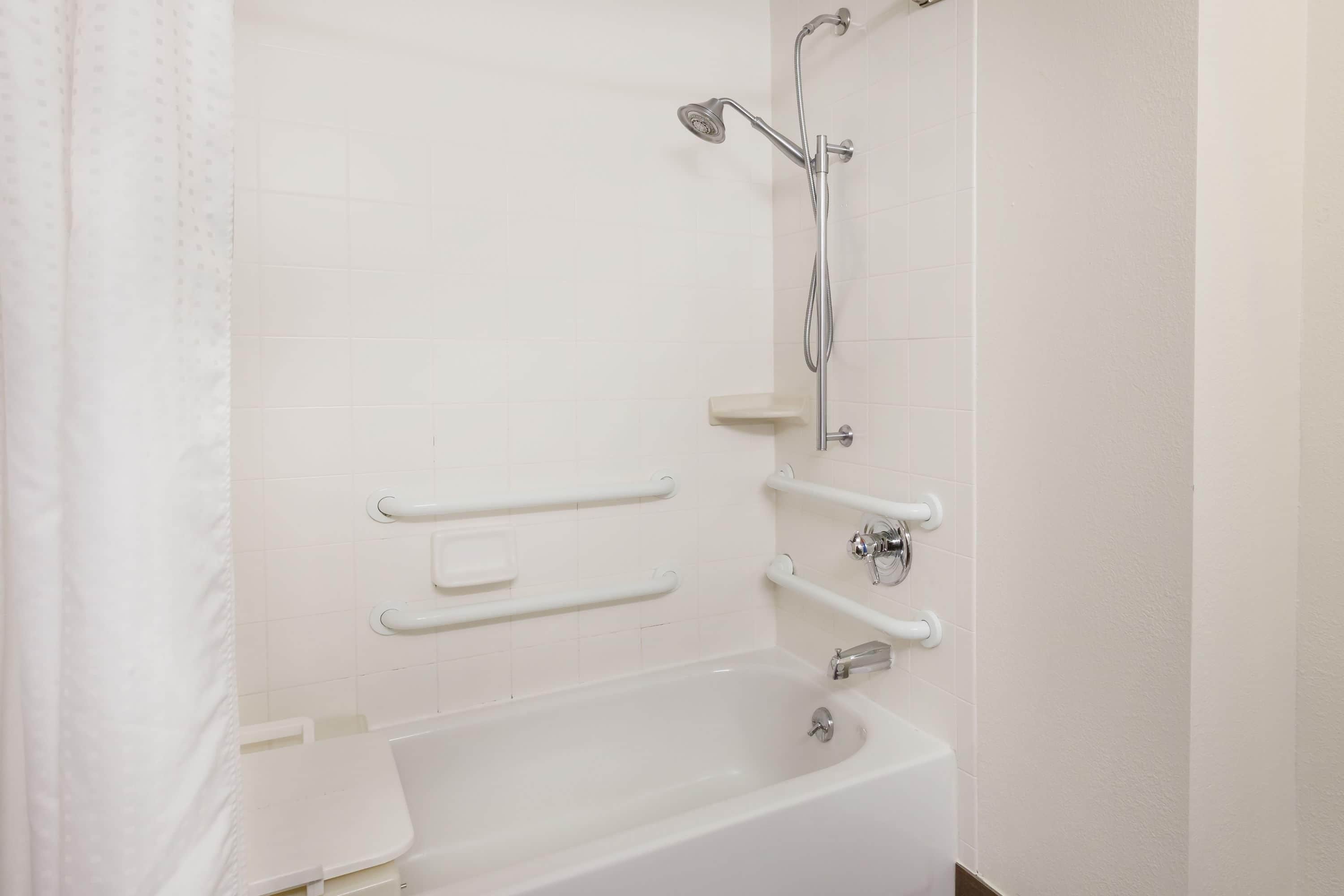 Une salle de bain avec une baignoire blanche, des barres d’appui et une pomme de douche.