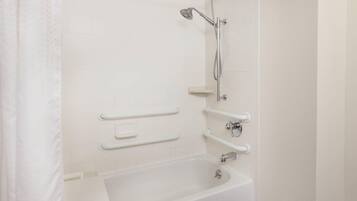 A bathroom with a white bathtub, grab bars, and a shower head.