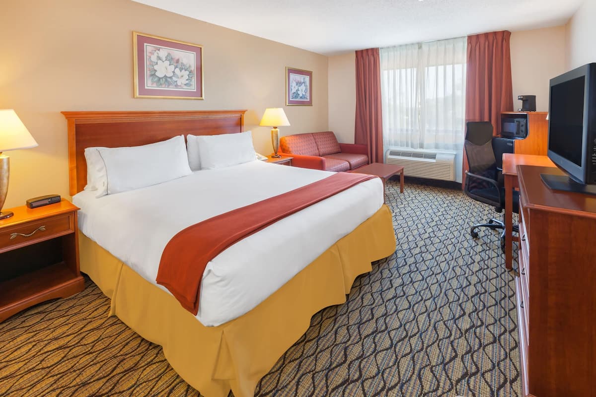A hotel room with a large bed, a desk with a television, a chair, and a sofa.