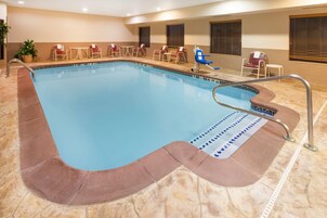 Una piscina interior con borde de azulejos, sillones de descanso y una pequeña mesa.