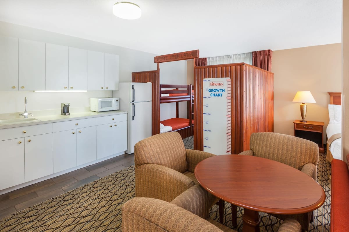 A hotel room with a kitchenette, a bunk bed, a dining table, and a lamp.