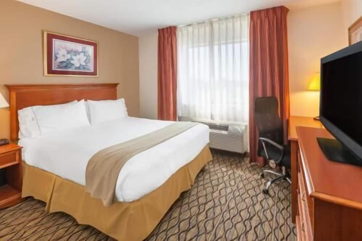 A hotel room with a bed, a desk, a chair, a television, and a window with curtains.