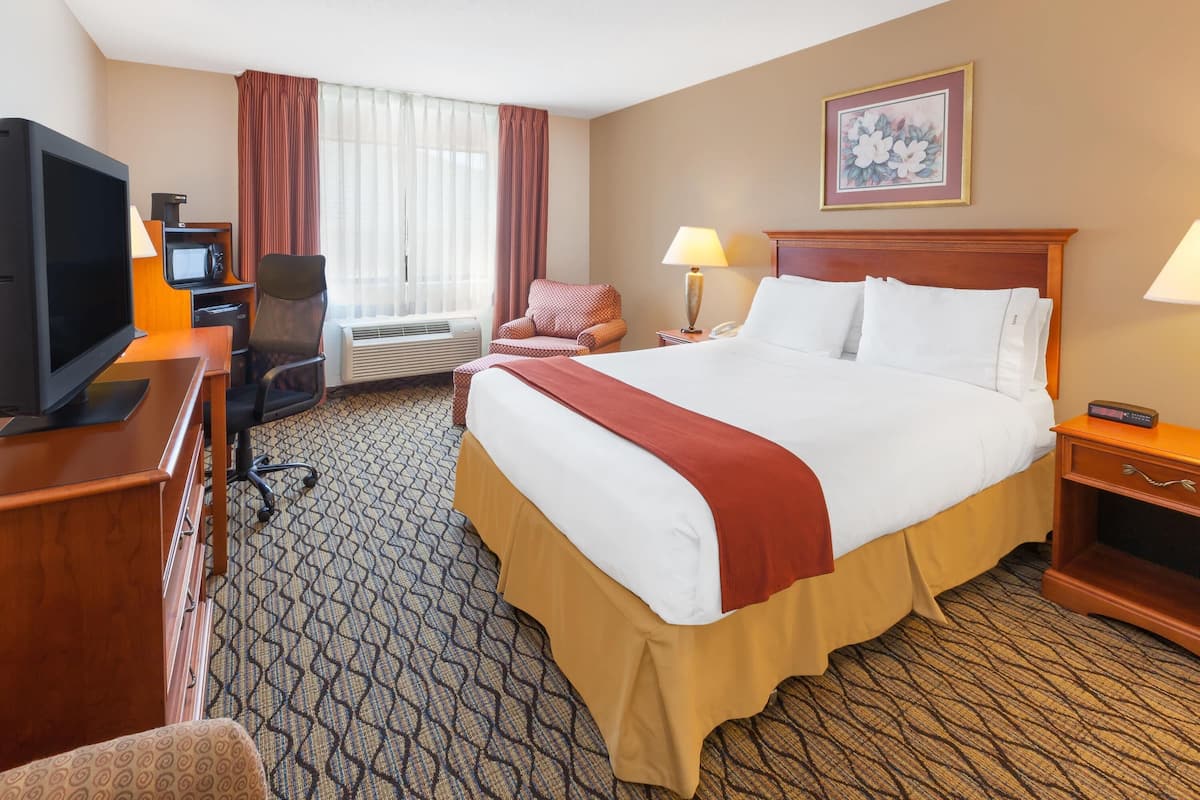 A hotel room with a bed, desk, television, chair, and a window with curtains.