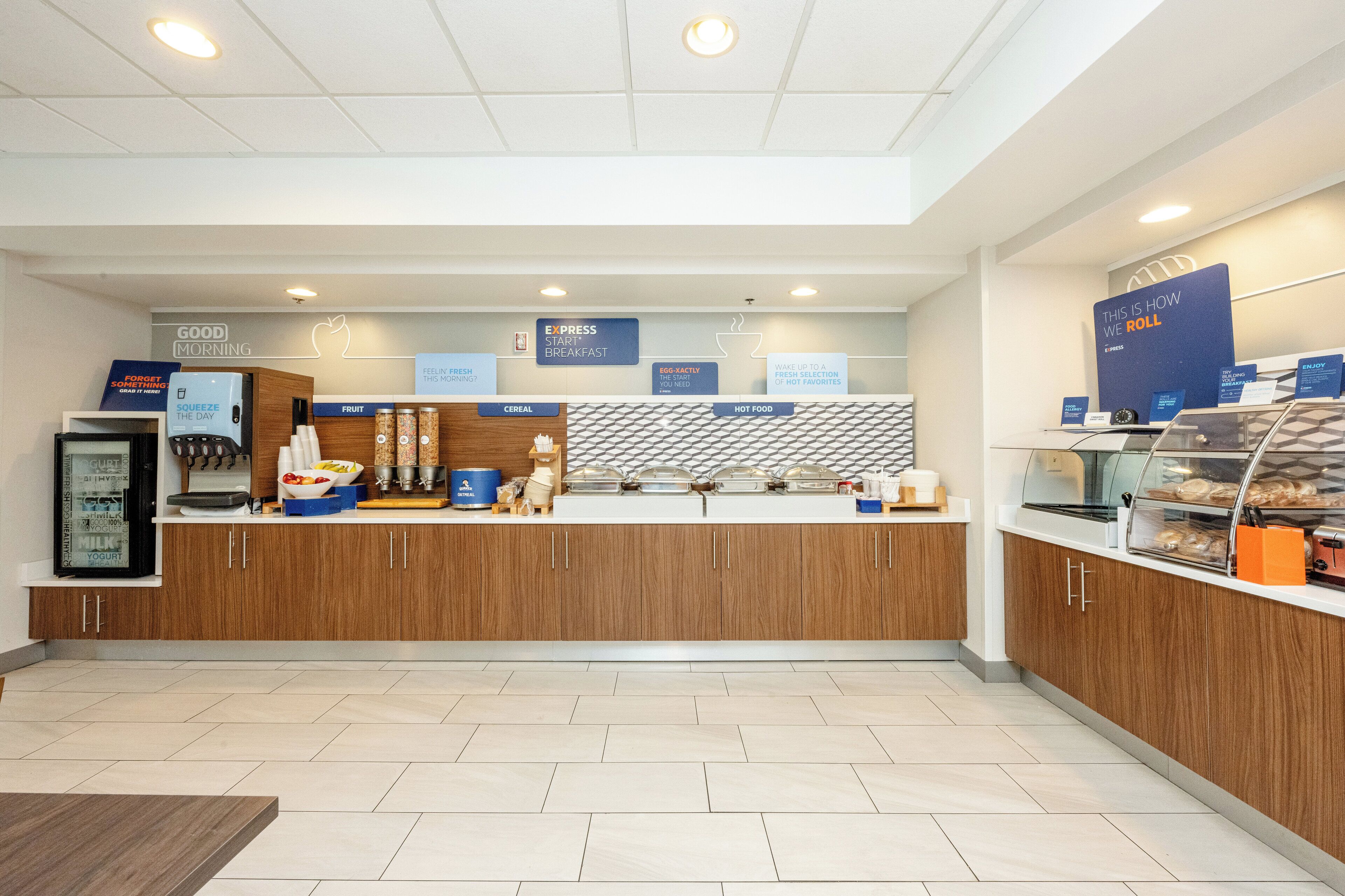 A modern breakfast area with a counter, various food options, and a sign indicating the breakfast menu.