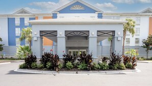 Un hotel con entrada central, varios pisos y un jardín frontal ajardinado.
