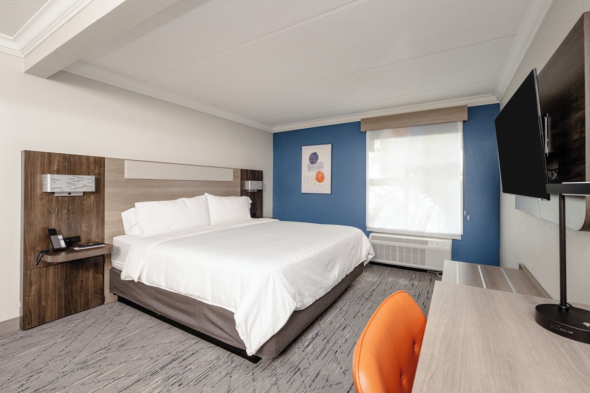 A hotel room with a bed, a desk, a chair, a TV, and a window.