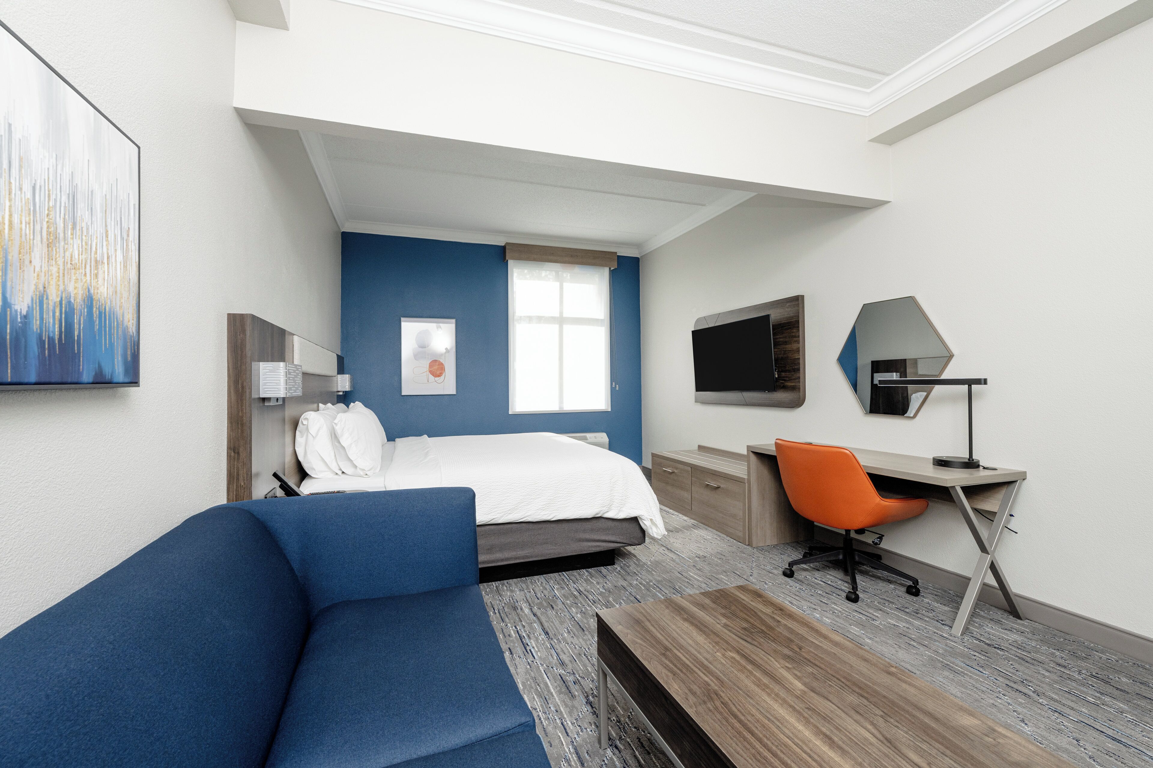 Una habitación de hotel moderna con cama, sofá azul, escritorio y televisor.