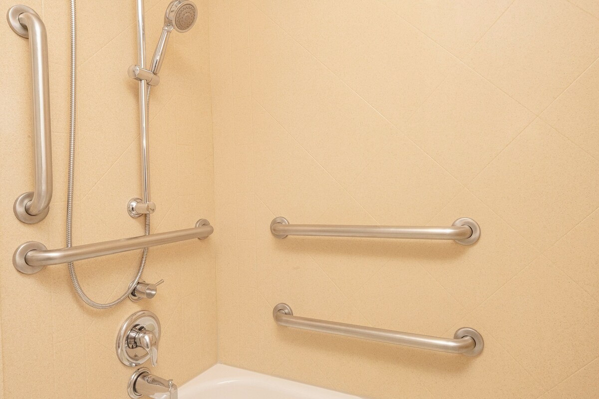 A bathroom with a bathtub, a shower with a handheld showerhead, and two grab bars installed on the wall.