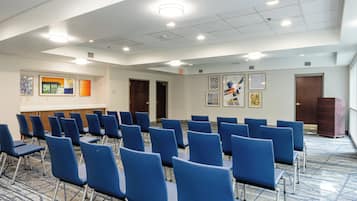 Un salón de conferencias con filas de sillas azules, un atril y obras de arte enmarcadas en las paredes.
