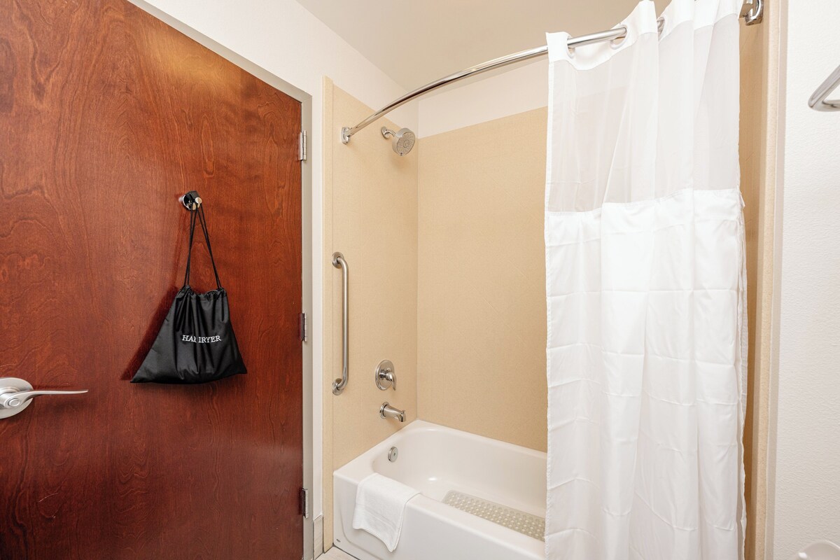 A bathroom with a wooden door, a white bathtub, a shower curtain, and a black bag hanging on the door.