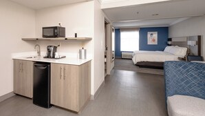 Habitación de hotel compacta con kitchenette, una cama, una mesita de noche y vistas al exterior.