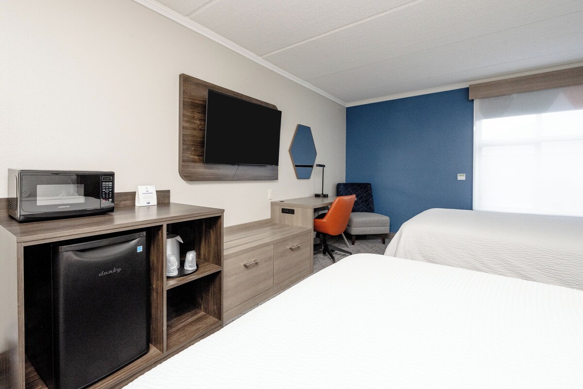 A hotel room with a bed, a desk with a microwave, a refrigerator, a TV, and a chair.