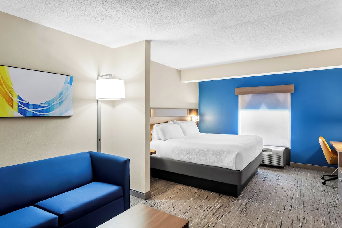Une chambre d’hôtel avec un lit, un canapé bleu, un bureau et un tableau accroché au mur.