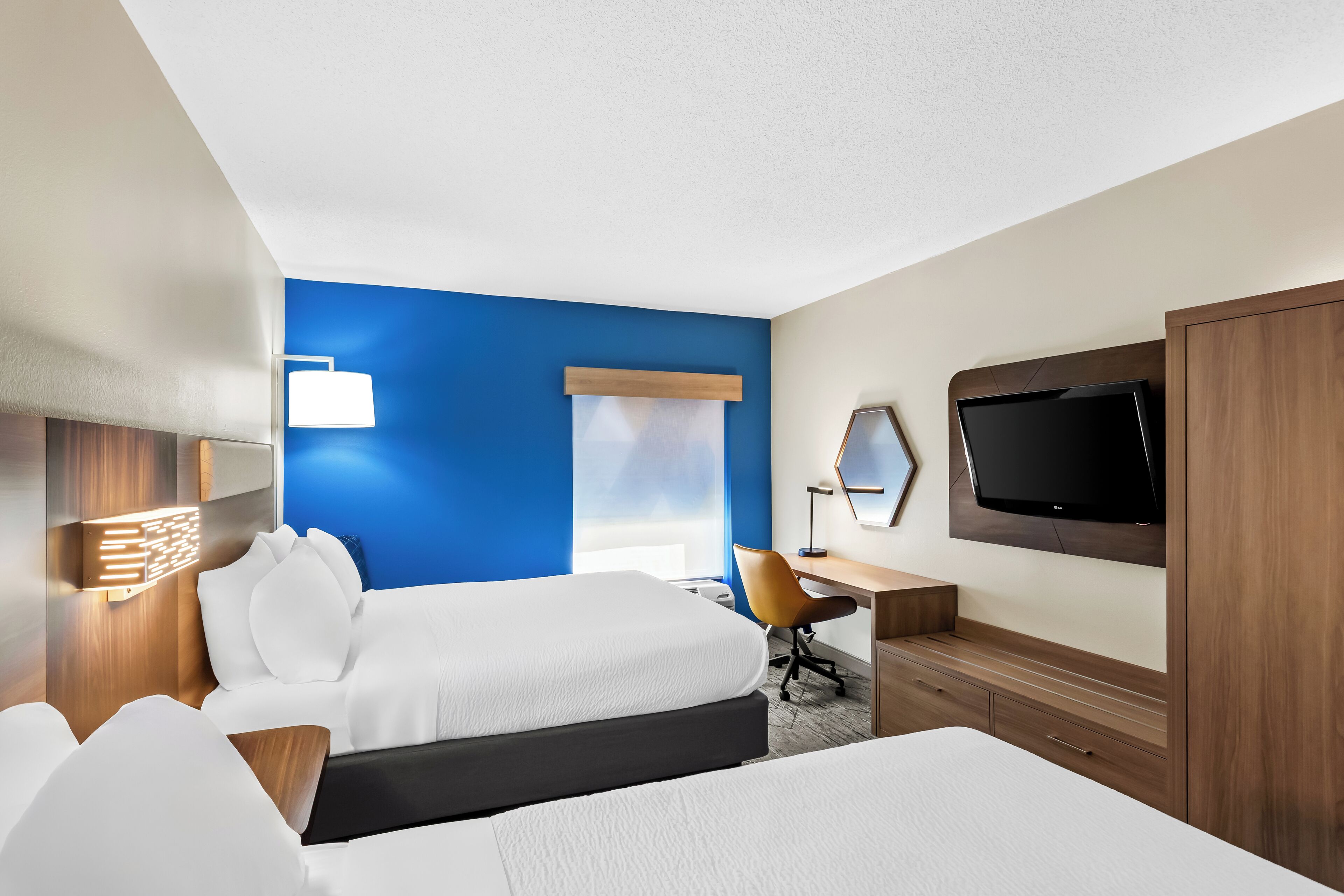 Une chambre d’hôtel avec deux lits, un bureau, une télévision et une fenêtre avec des stores.